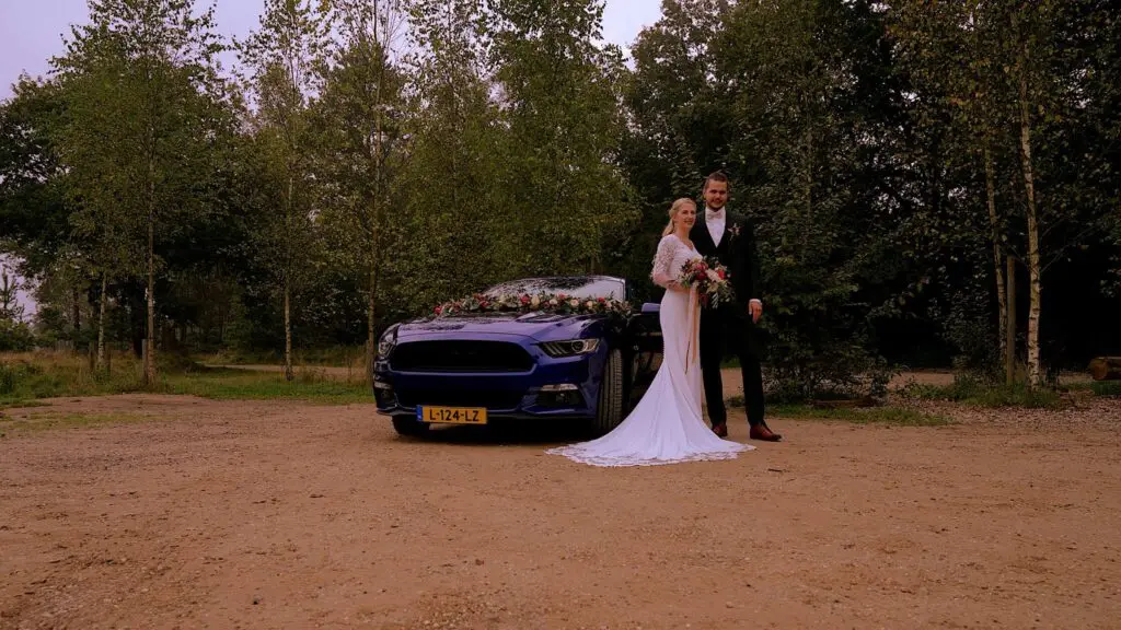 Trouwfilm Nunspeet - Bruidspaar poseert bij trouwauto.